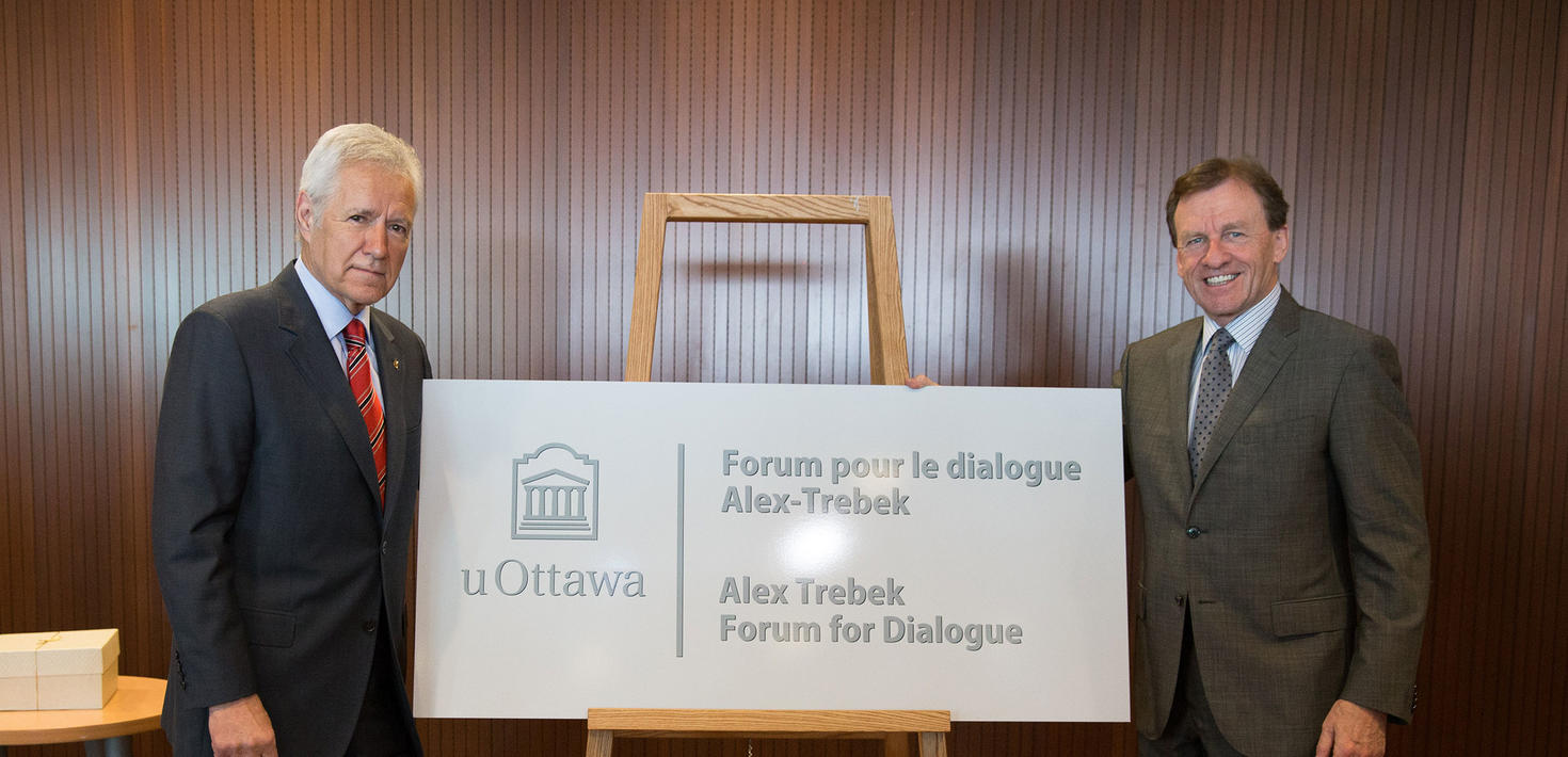 Alex Trebek et Allan Rock montrant un panneau sur un chevalet annonçant le Forum pour le dialogue
