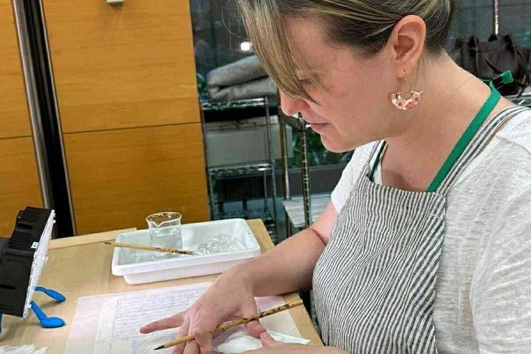 L’archiviste Gabriela Rosas, assise à une table, fait une intervention de restauration du papier.