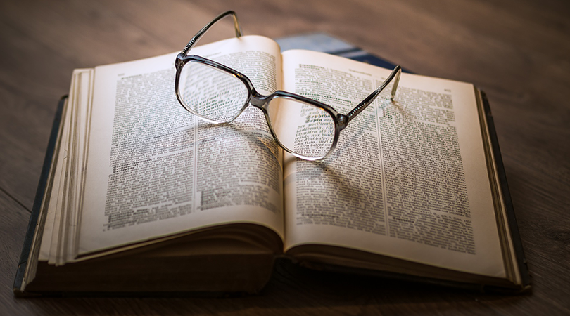 An open book with glasses resting on top.