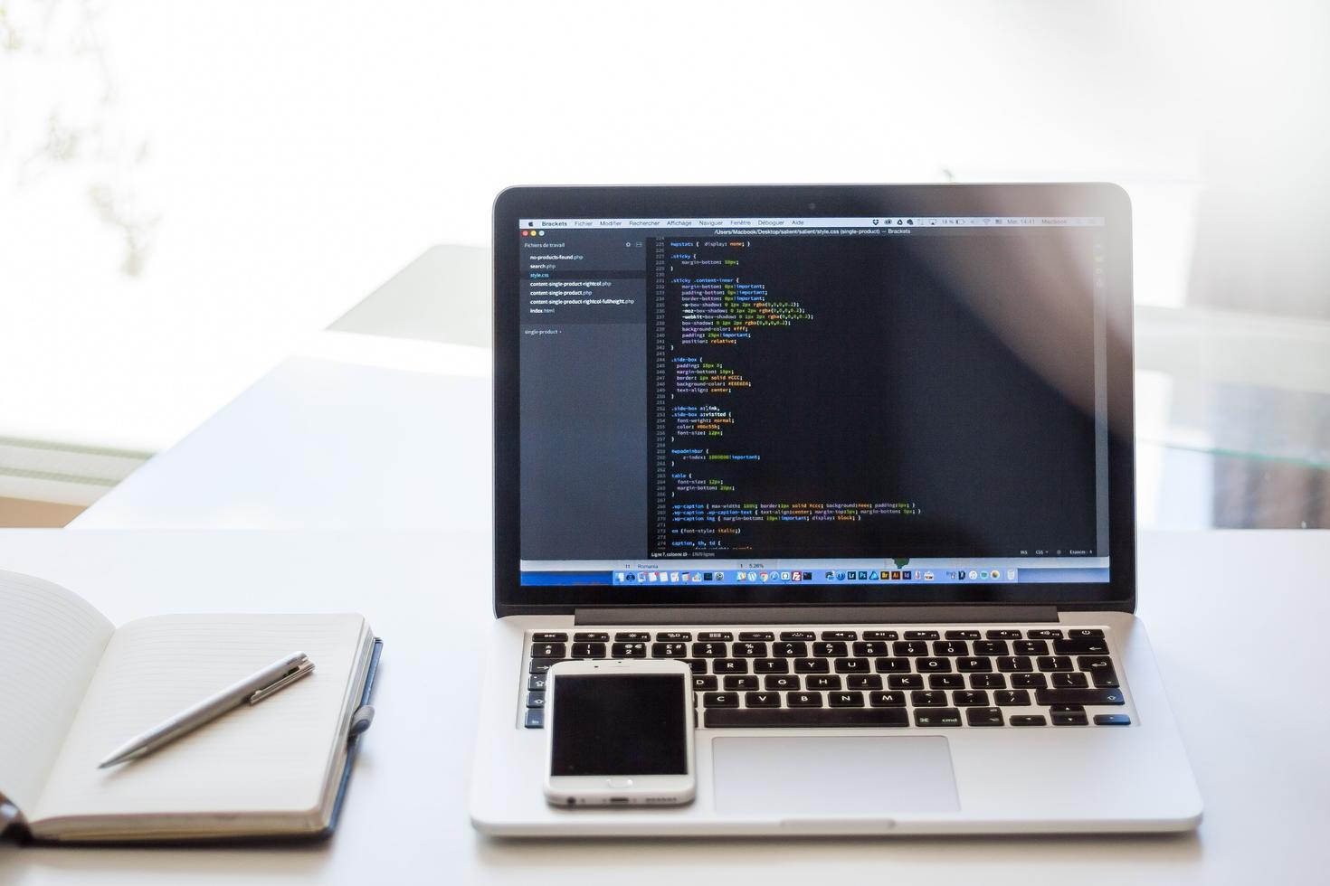 Photo of laptop on a desk besides a notebook