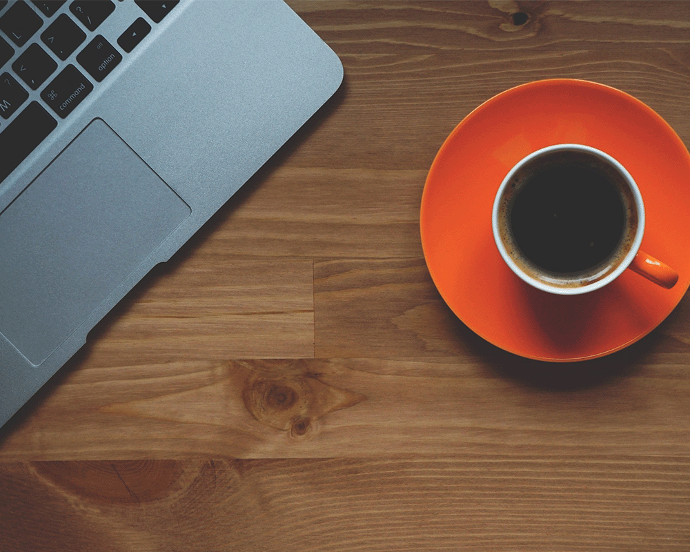 A cup of coffee next to a computer.
