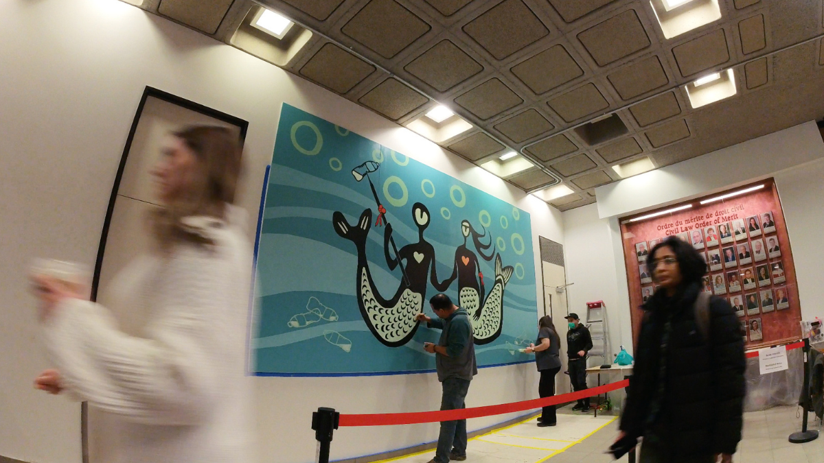 people painting a mural on the wall as students walk by.