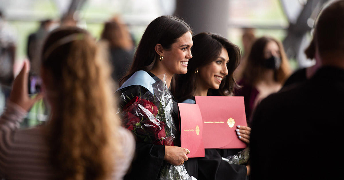 two women graduates hold their degrees smiling for a picture