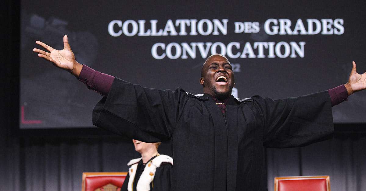 graduate cheering on stage with arms spread out wide