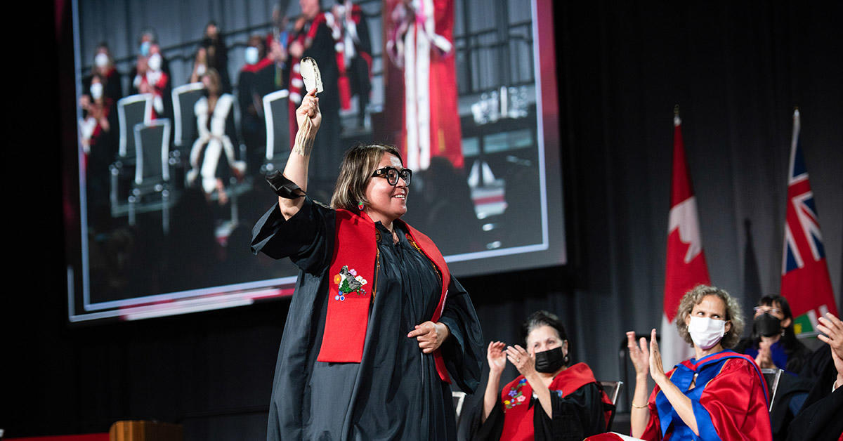 an indigenous law student crosses stage holding a feather in one hand