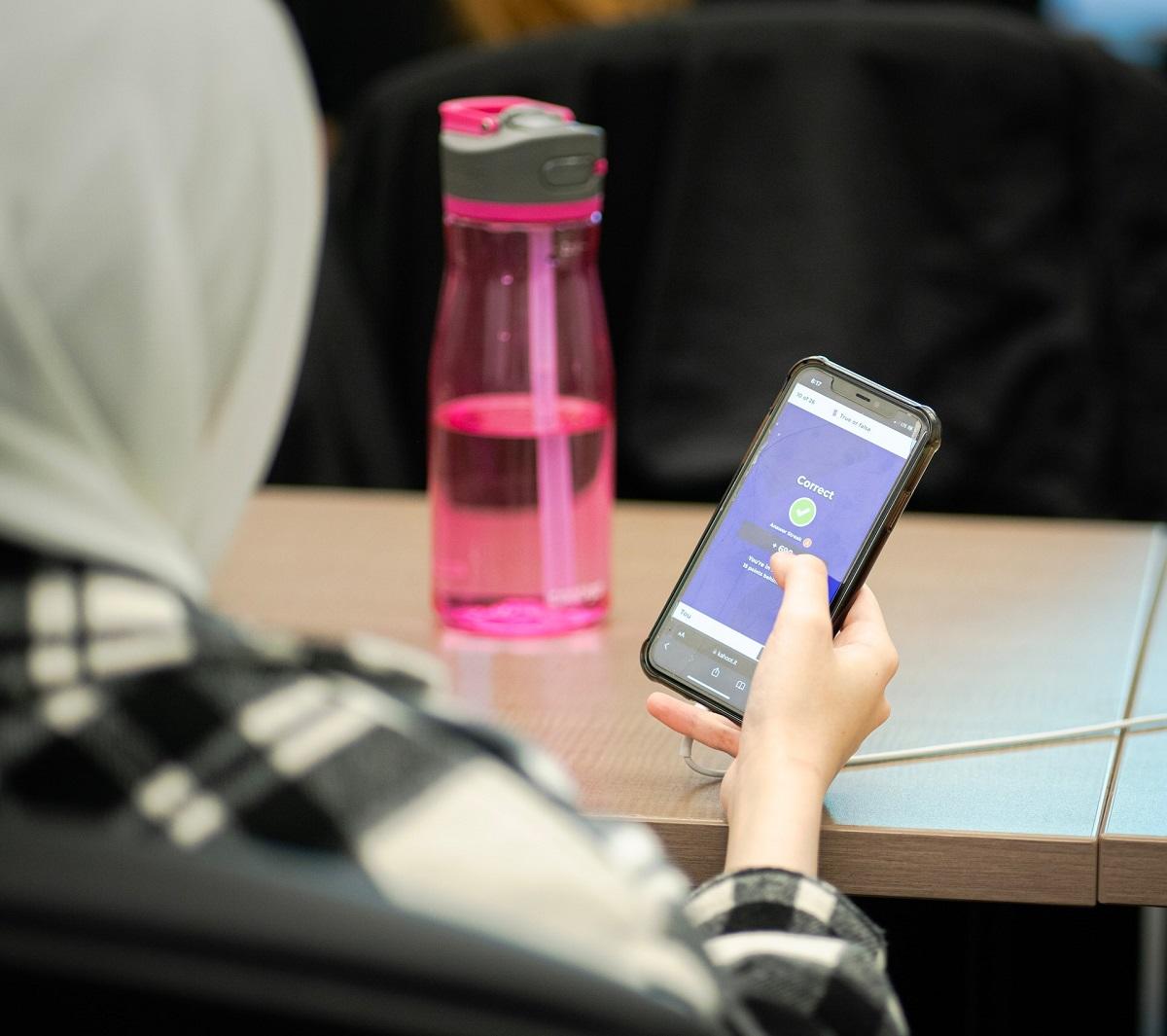 Fille en hijab tenant un téléphone portable dans une salle de classe
