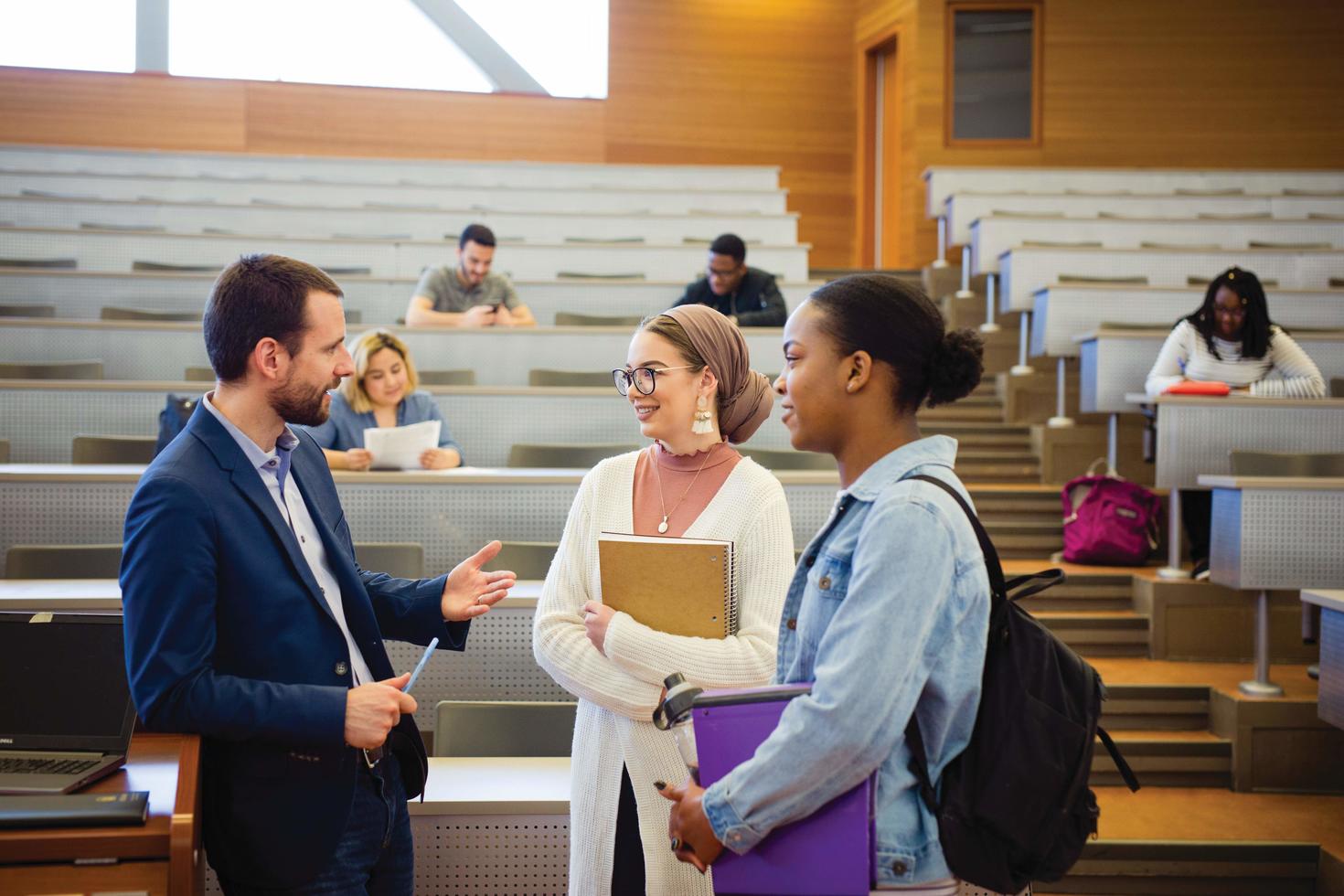 Students speaking with a professor in a classroom. 
