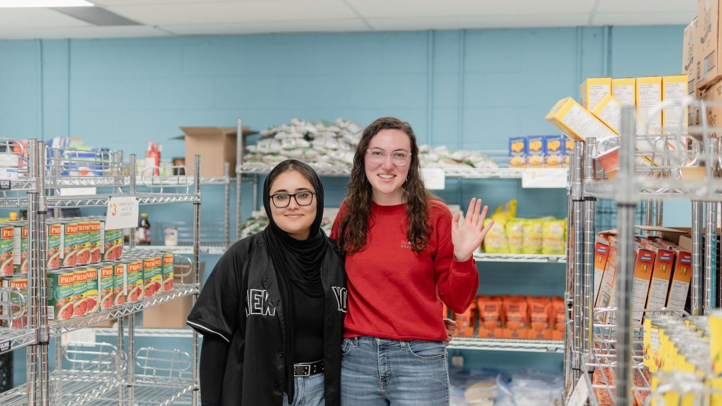 Deux étudiantes bénévoles devant les étagères remplies de nourriture de la banque alimentaire du syndicat étudiant de l'Université d'Ottawa.