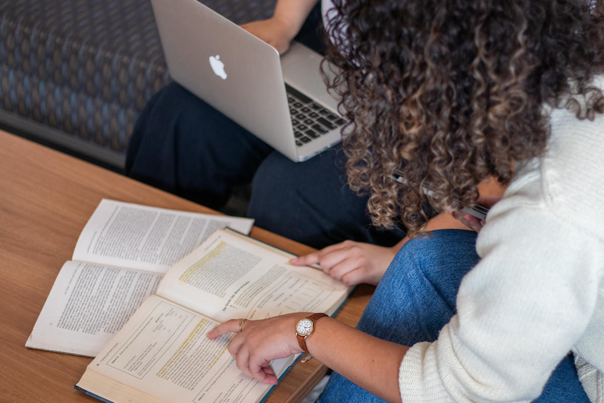2 students studying with a laptop and a book