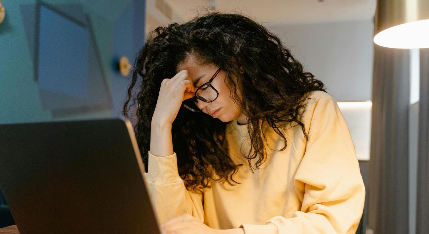 A student looks stressed out. She rubs her forehead as she looks at a laptop.