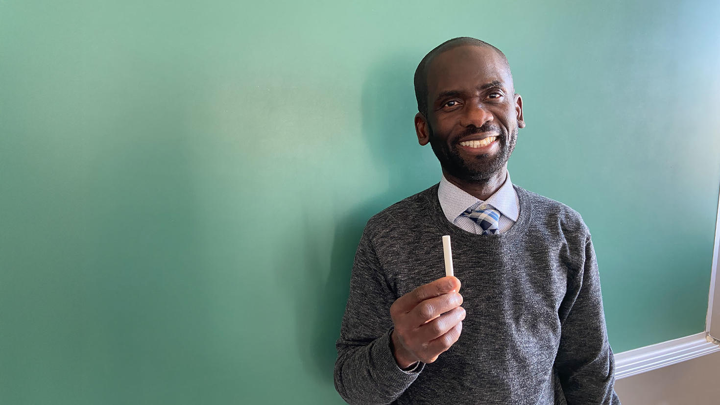 Person standing in front of a chalk board, holding a piece of chalk