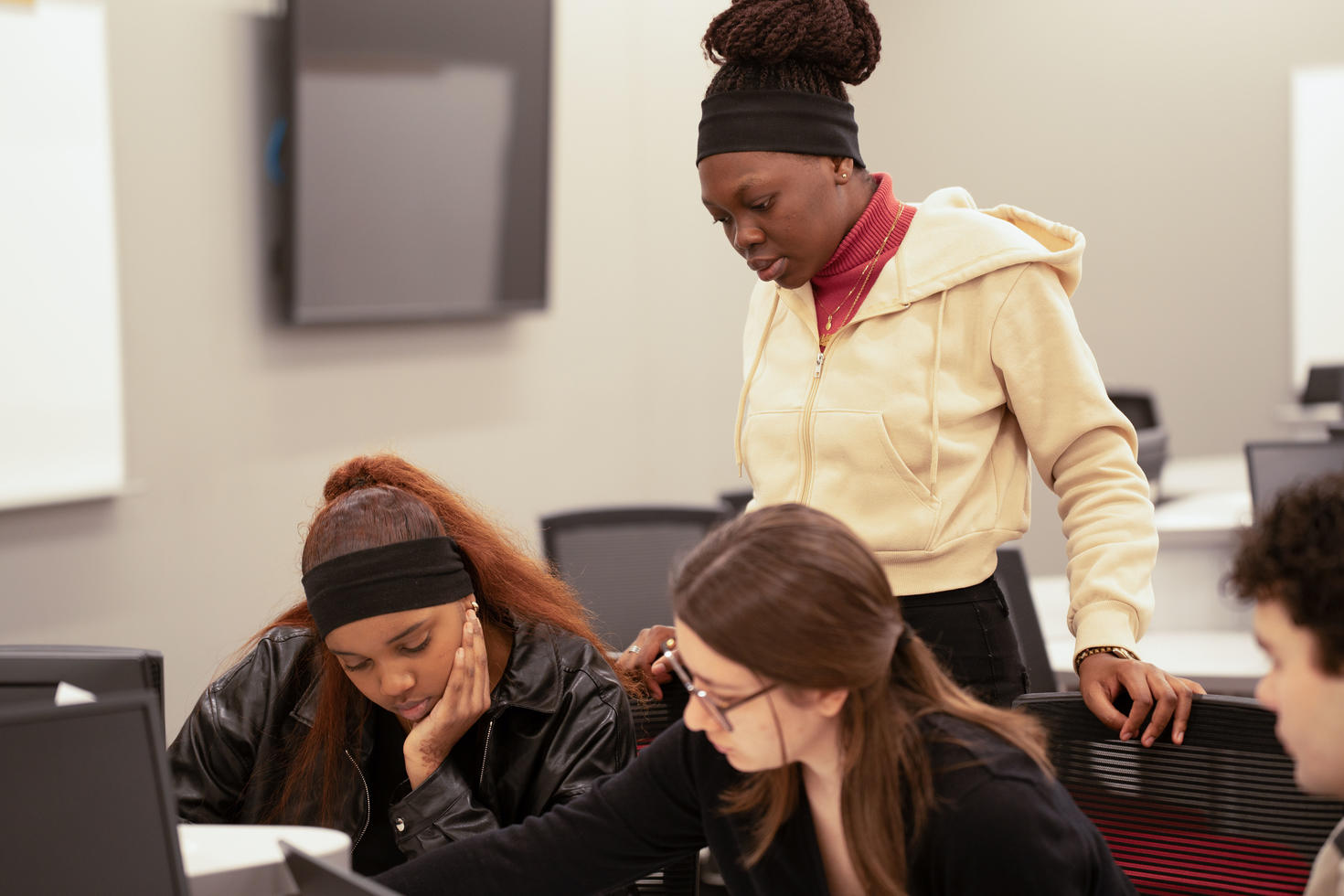 Three students collaborating in front of a computer screen.