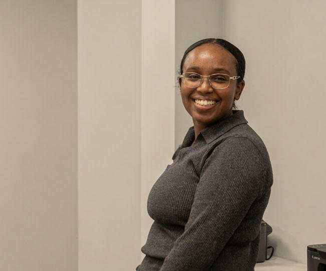 A person stands sideways to the camera, face turned to the camera and smiling
