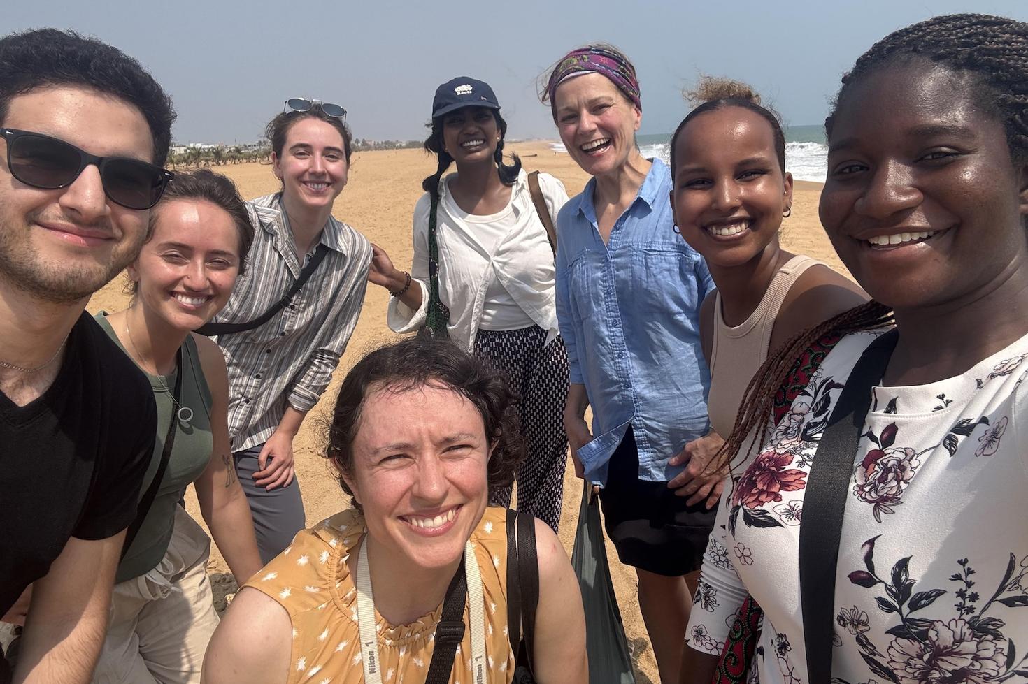 Huit apprenants et enseignants posent ensemble dans un lieu international au paysage sablonneux.