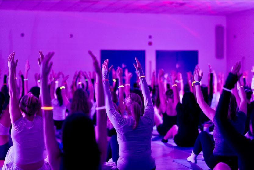 Une salle remplie d'étudiantes et étudiants pratiquant le Pilates, les bras levés en l'air, lors d'un événement fluorescent.