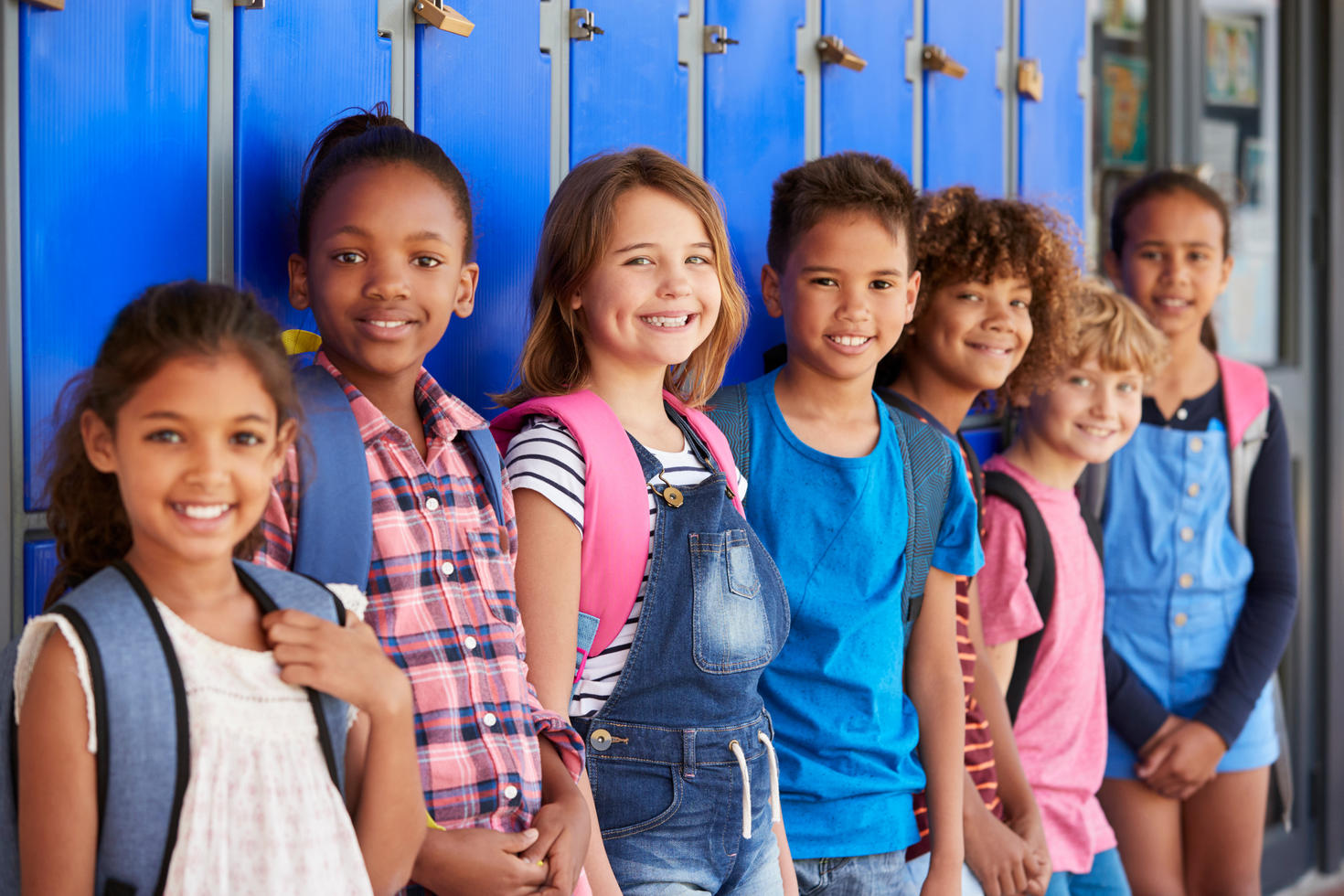 Young students with backpacks in front of school lockers.