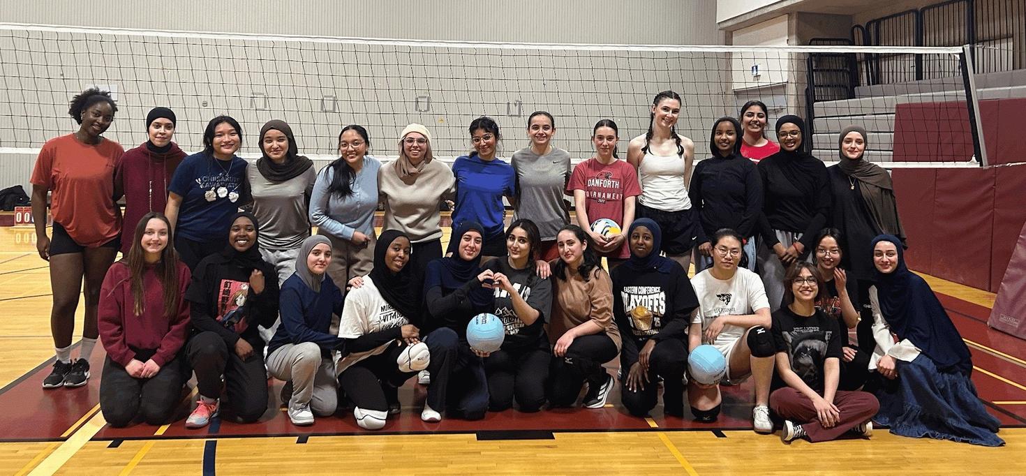 Plus de 20 membres du club WeSport de l'Université d'Ottawa posent en groupe dans un gymnase, devant un filet de volley-ball.