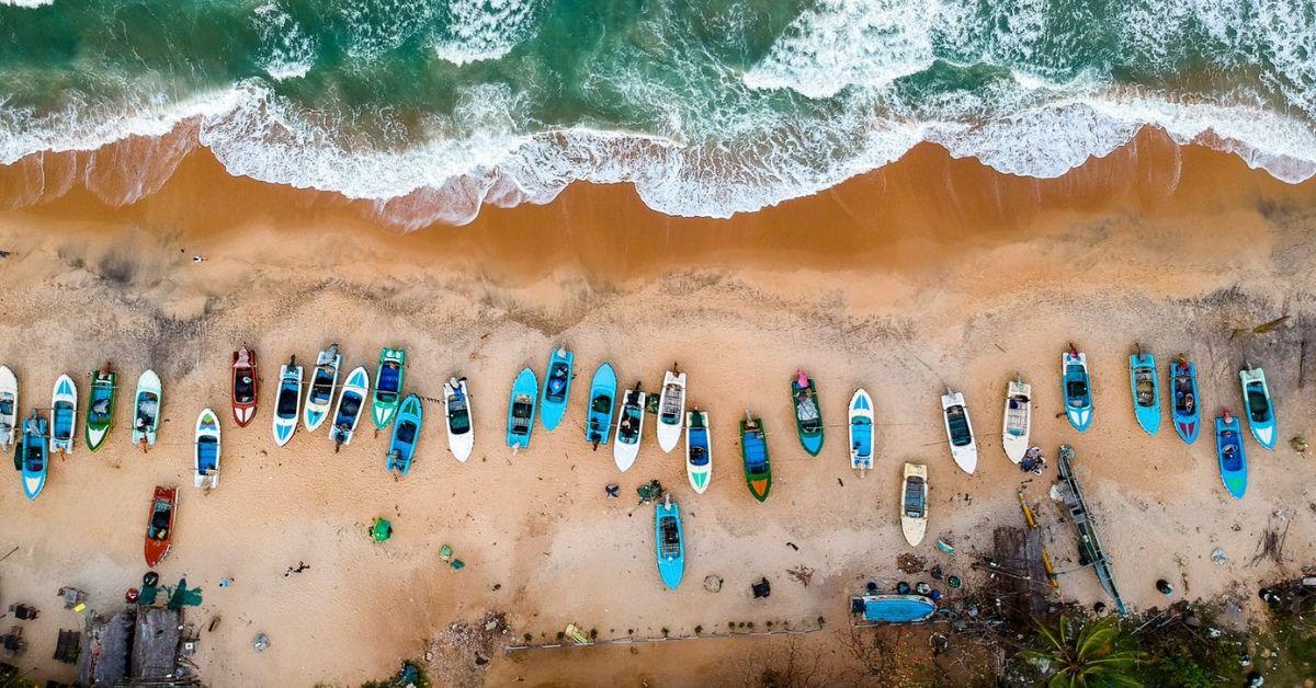 A bird-eye view of a beach with a canoes of different colours lineup on the beach