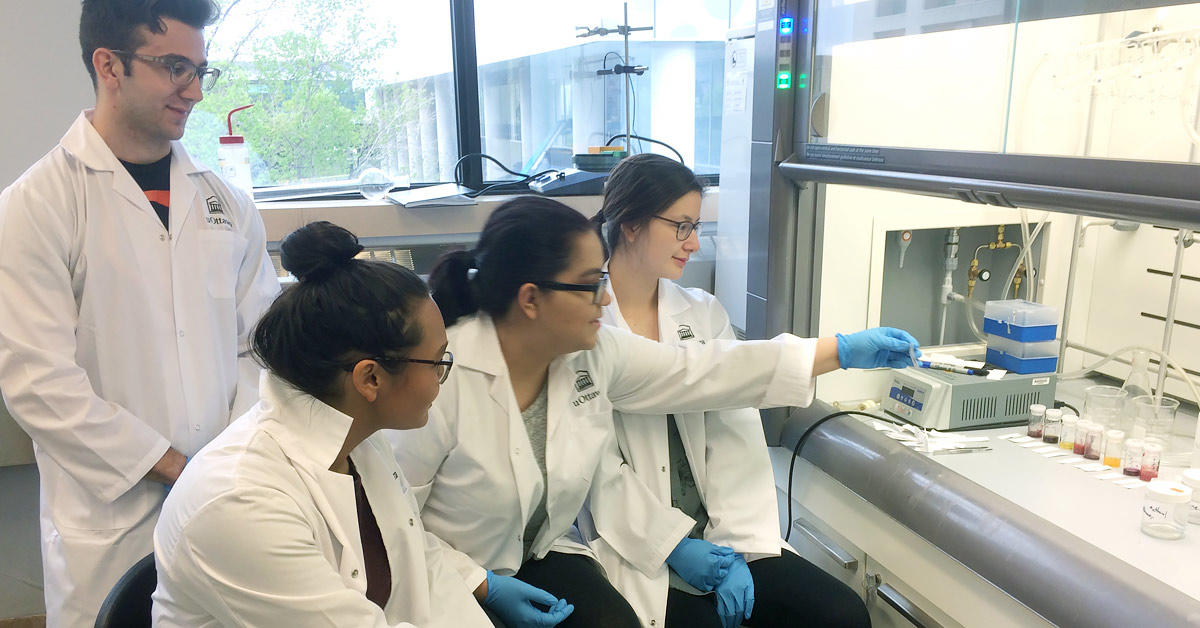 Students in lab coats in a biochemistry lab with test tubes.