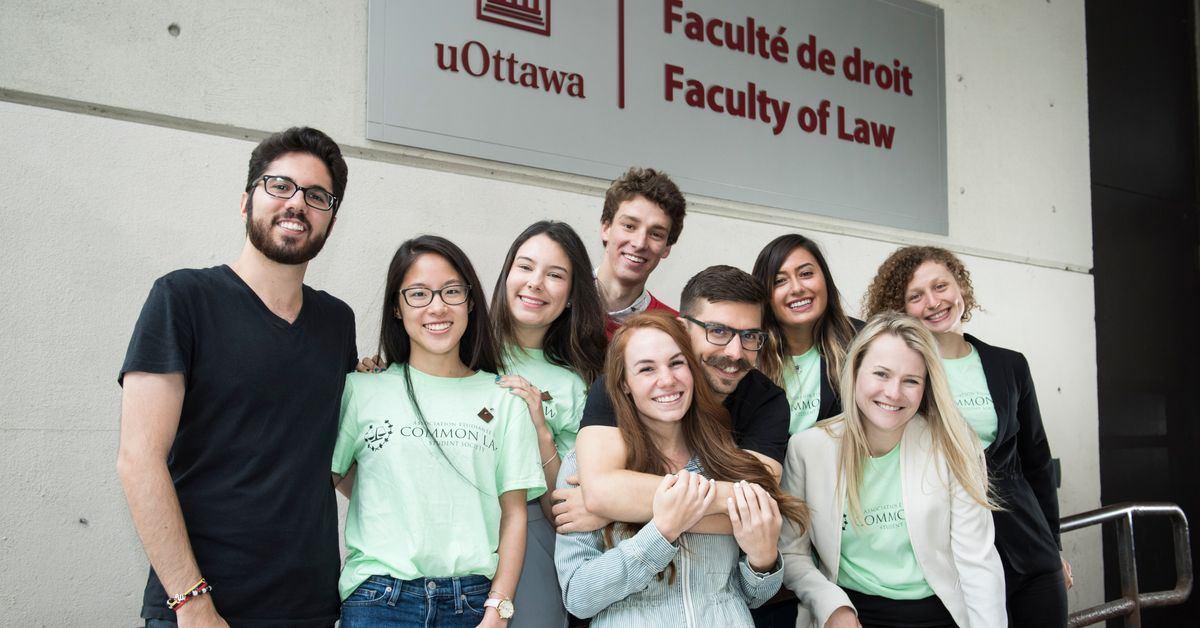 Des étudiants en droit posent debout devant l'enseigne de la Faculté de droit.