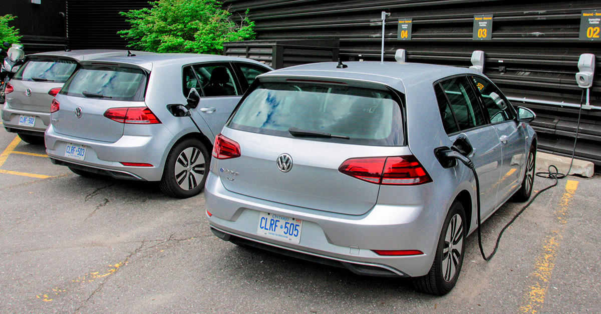 Three electric Volkswagen cars parked in a row and plugged into wall chargers