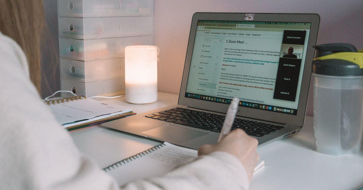 The hands of a woman holding a pen while sitting in front of a laptop.