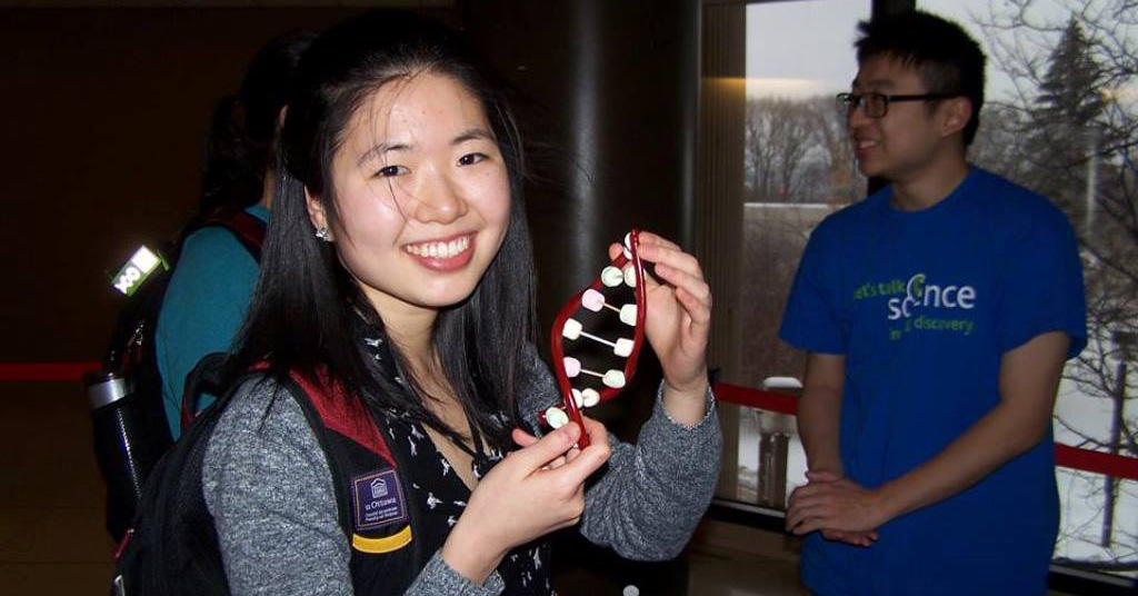A young woman proudly displays a model of a double helix.