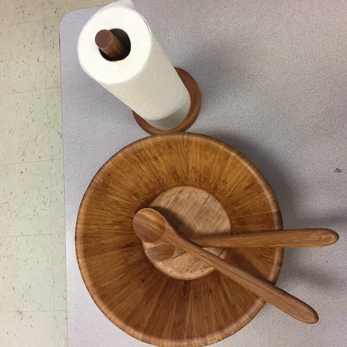 Un saladier en bois avec deux cuillères et un rouleau de serviettes en papier.