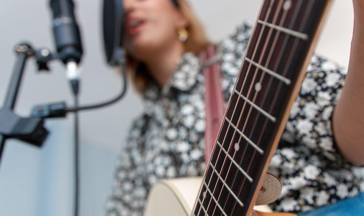 A woman playing the guitar while singing into a microphone.