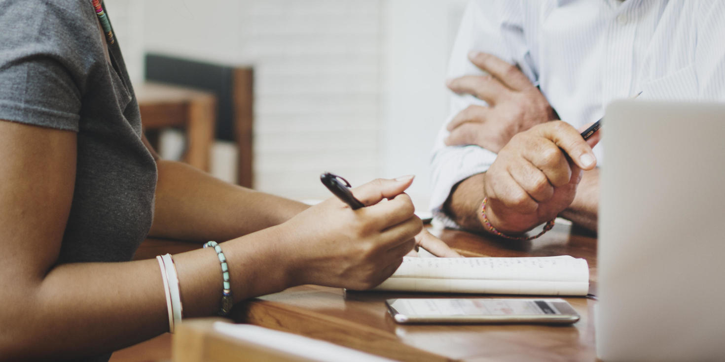 picture of two people sitting at a desk holding a pen and paper