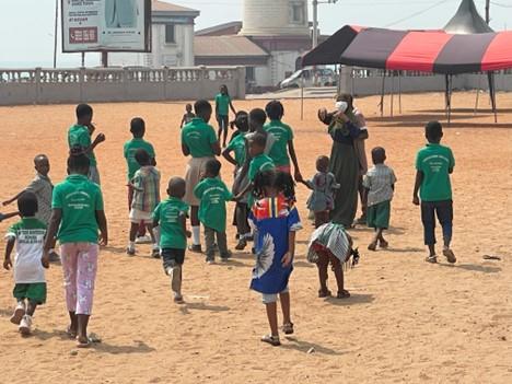 Un groupe d'enfants portant un t-shirt vert et marchant sur le sable dans un village