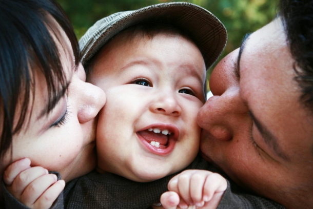 Deux parents embrassant les joues de leur enfant.