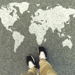 A person's feet standing in front of a world map drawn in white on the ground 