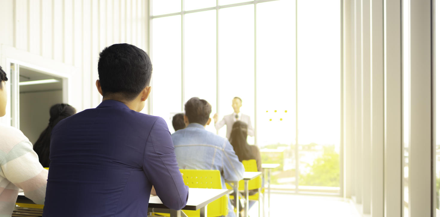 row of people in desks in bright sunlight facing a speaker