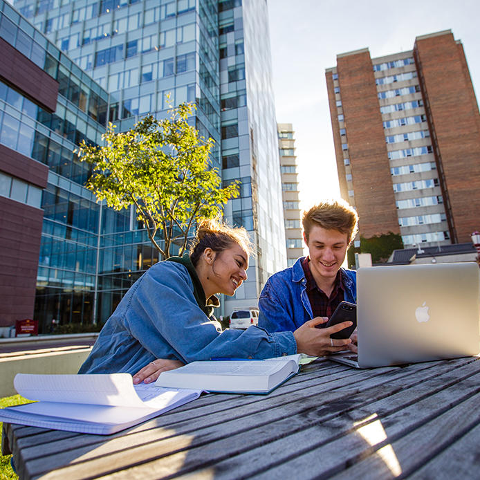 Students siting outside studying in sunshine near Faculty of Social Sciences building. 