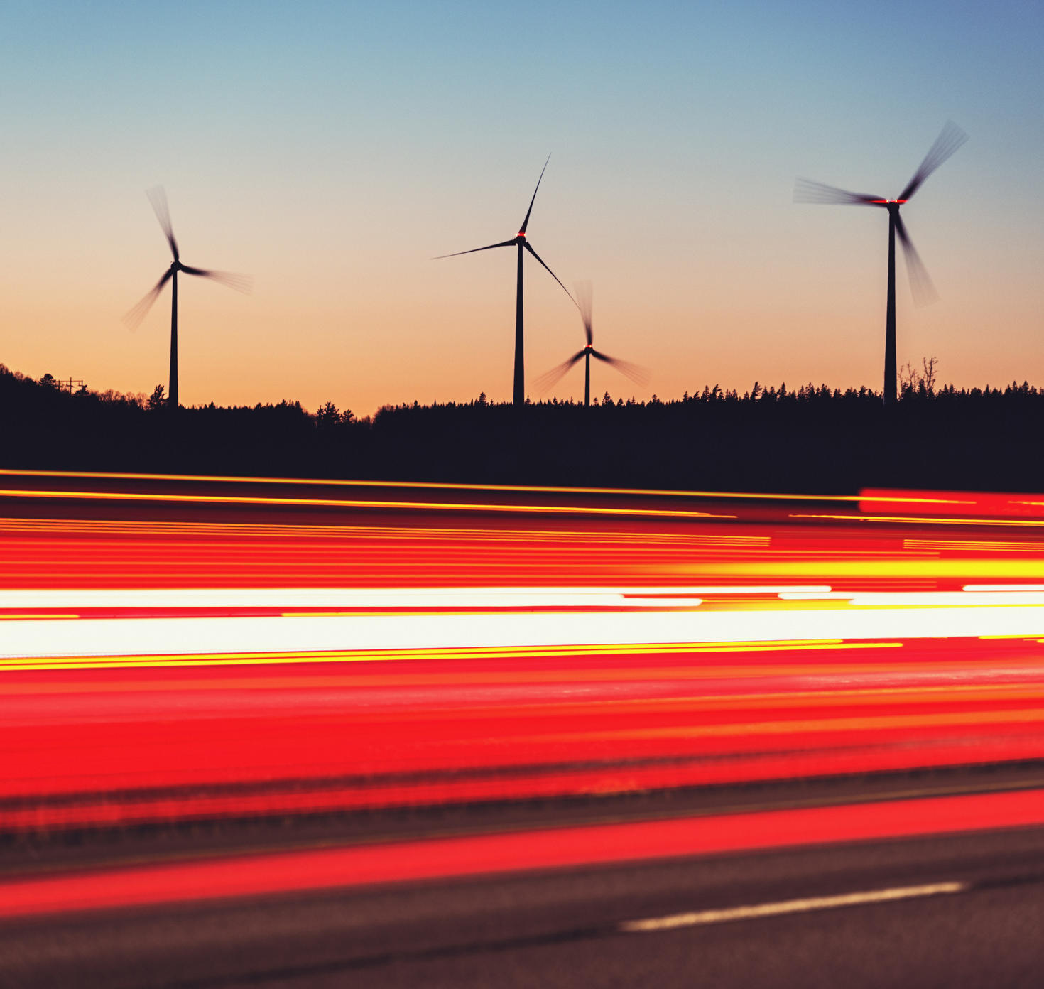 A trail of lights on a road with silhouettes of windmills in the background