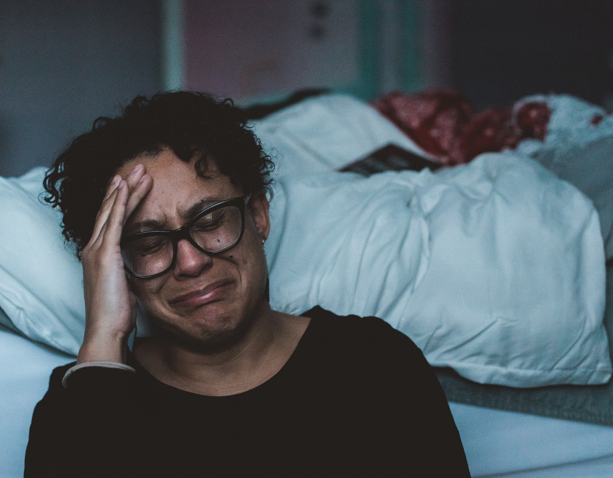 Woman seated on floor beside bed crying
