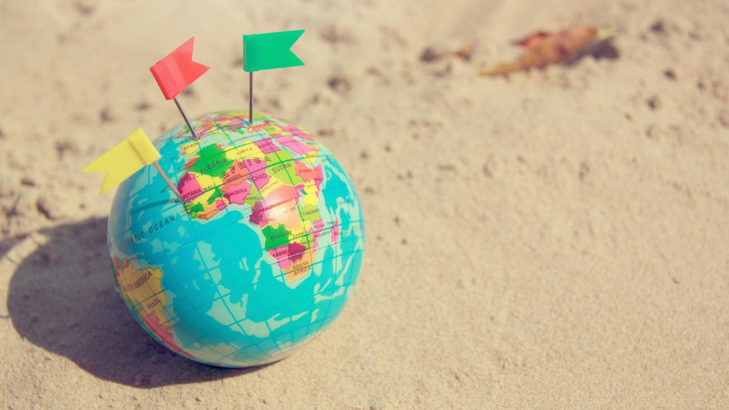 globe of world with three coloured flags lying on sand