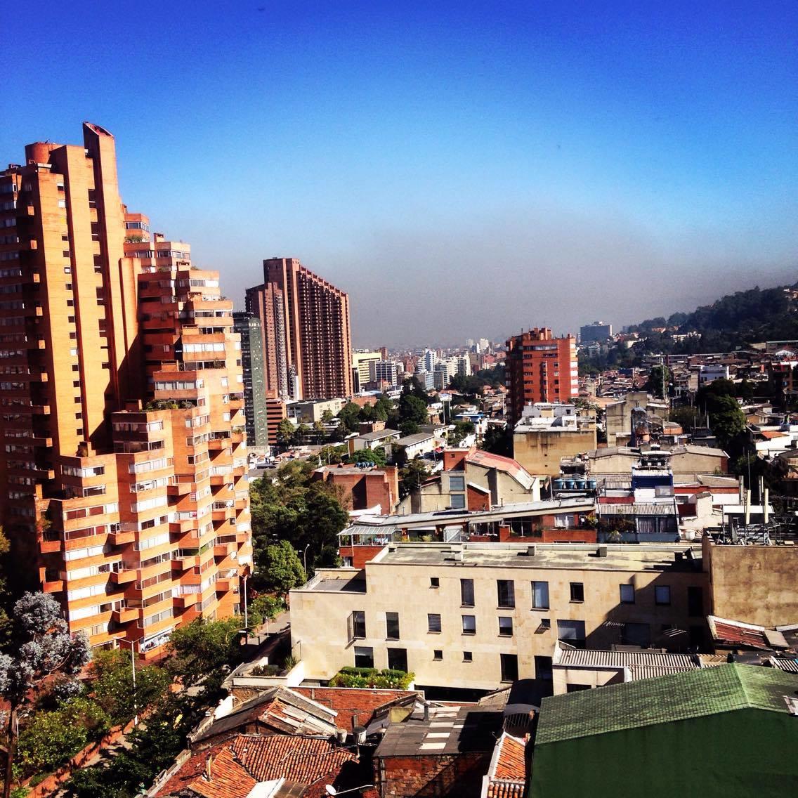 A neighborhood viewed from the rooftop of a buildin. Multiple buildings of different size and different colors(generally white, orange and green)