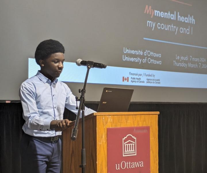 High school student David Tercy gives a presentation behind a podium with a computer and a mic to highlight the importance of an event dedicated to Black community youth and the racial challenges they face.
