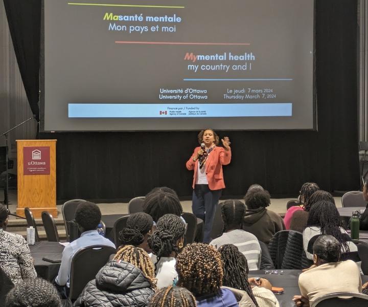 Senator Bernadette Clément gives a presentation to a roomful of high school students in Huguette-Labelle Hall at the University of Ottawa. The senator is describing her political career and the challenges related to the intersectional aspects of her identity. 