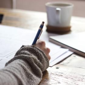 person writing with mug