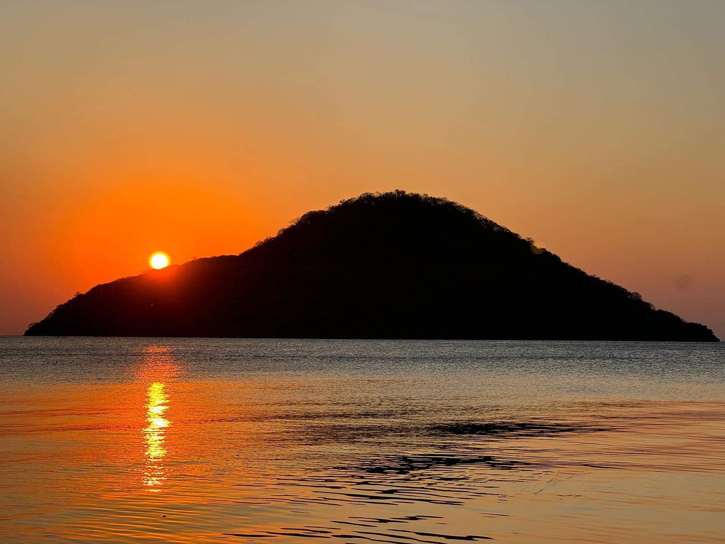 A hillside landscape at sunset overlooking the sea.