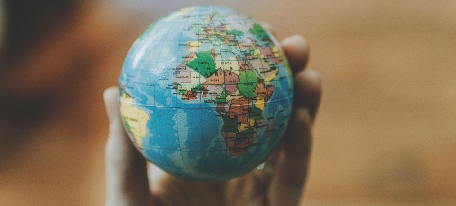 Small world globe with view of Africa, Europe and tip of Brasil, held in a person's hand.