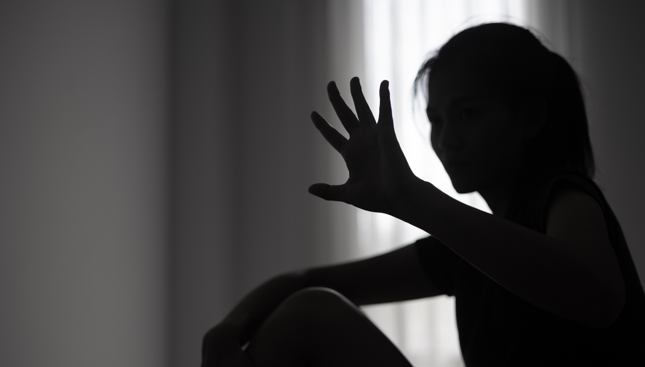 Silhouette of a young person sitting near a window, with one hand raised in a protective gesture.