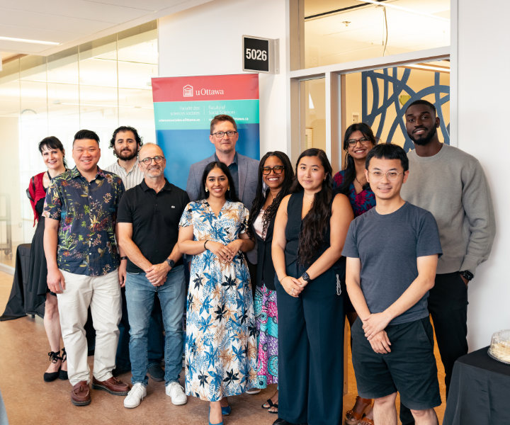 Faculty members, staff, and students stand together outside the entrance of the affinity space for a group photo. A Faculty of Social Sciences banner is displayed beside the doorway, with refreshments visible nearby as part of the opening celebration.