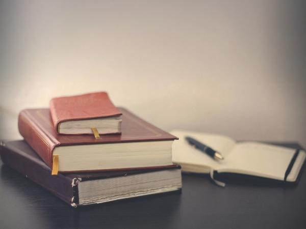 Three stacked books and a pen on an open notebook. 