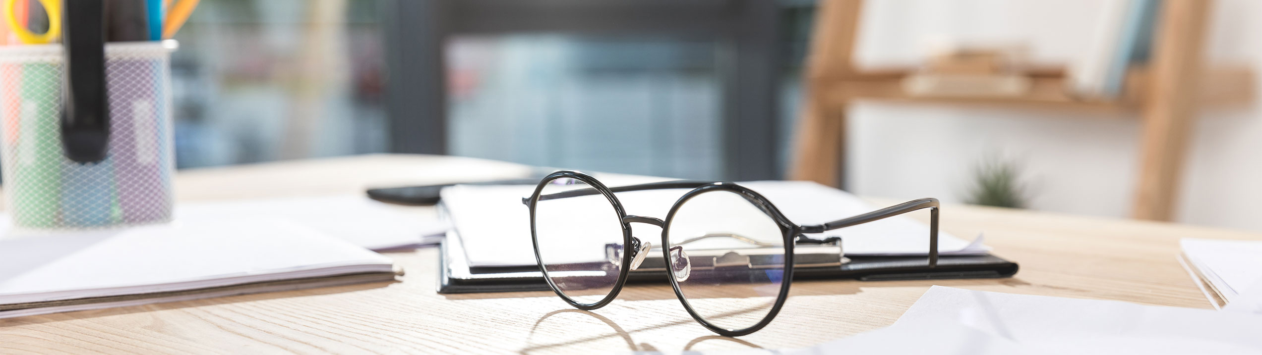 Une paire de lunettes posée sur un cahier, sur une table en bois.