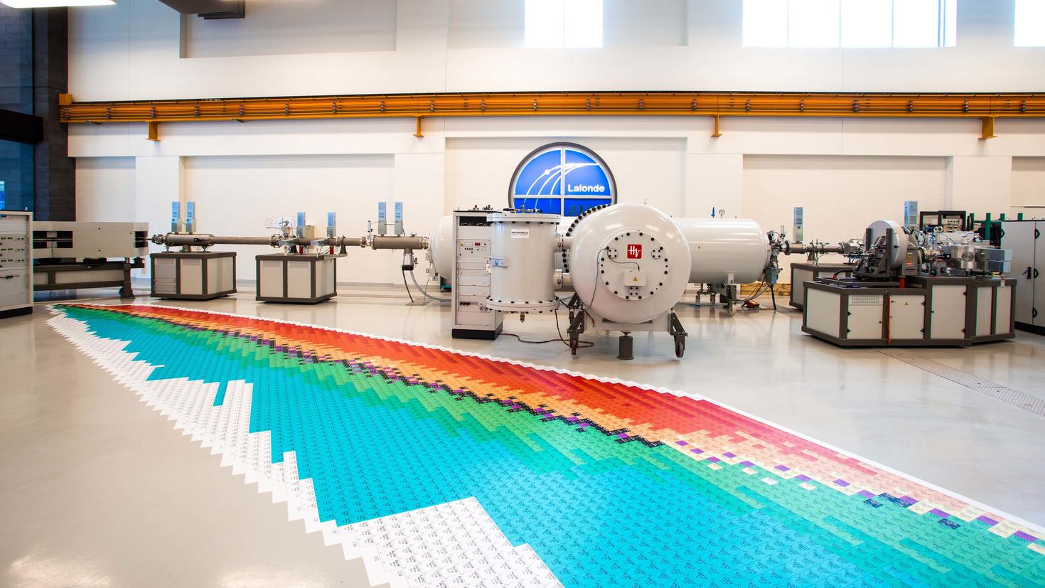 Intérieur d'un laboratoire montrant un spectromètre de masse par accélérateur et un gigantesque tableau périodique imprimé
