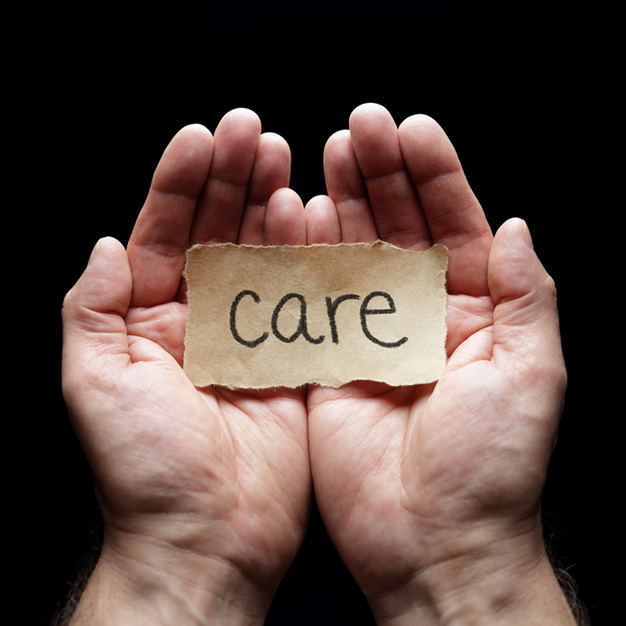 Le mot « care » sur un morceau de papier brun, dans une paume de main 